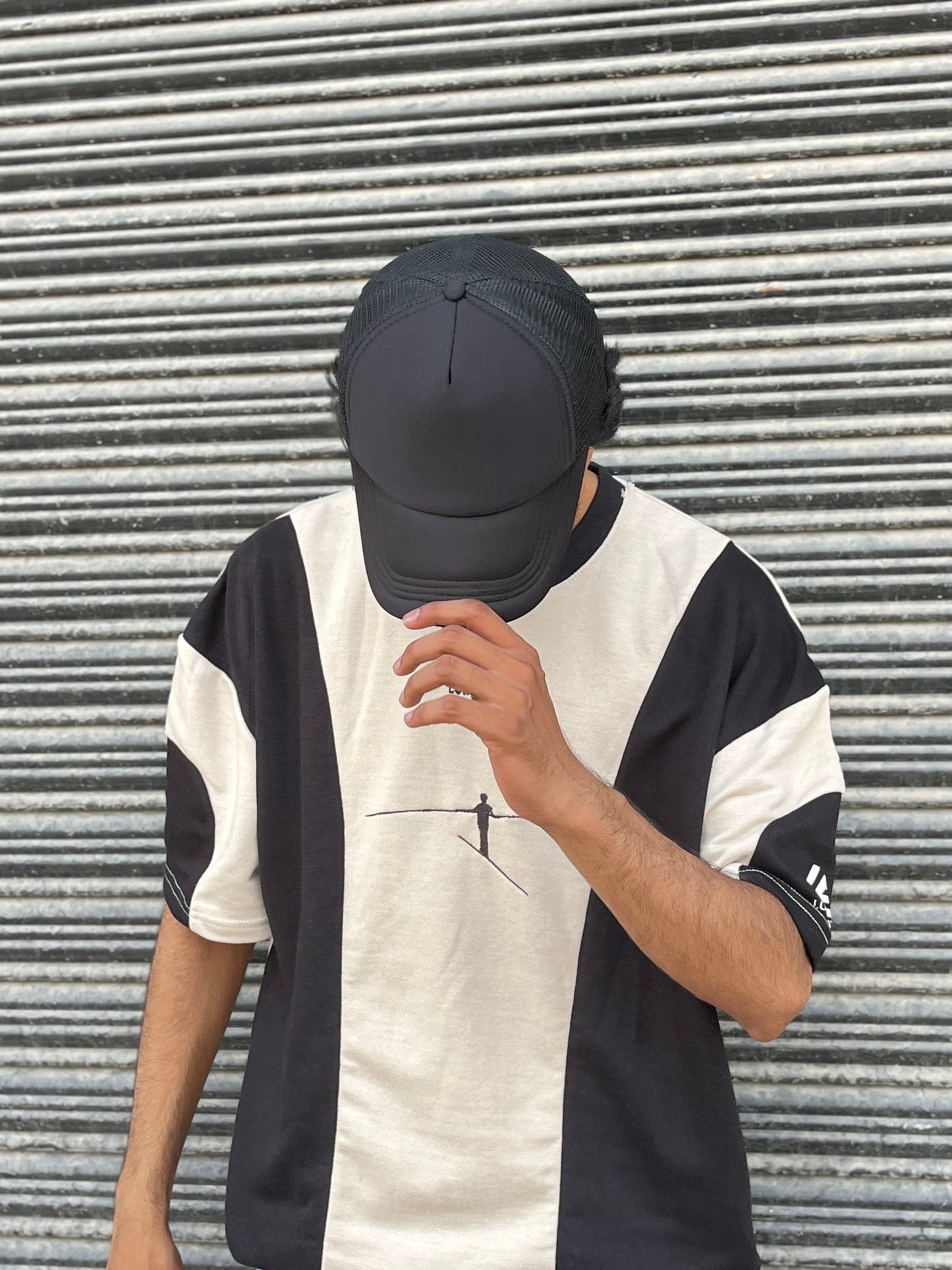 Man wearing a premium black trucker hat and black and white graphic t-shirt standing in front of a striped metal wall